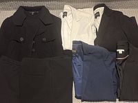 Overview of the lot showing the white, black, navy blazers laid out with the black short wool blazer coat and two pairs of dress pants.