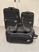 Front view of the two upright rolling suitcases and the carry-on duffel bag on carpeted floor, showing overall condition and matching black color with Skyway logos.