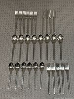 Photo showing all flatware pieces laid out on carpet: 10 dinner forks, 10 teaspoons (one bent), 6 smaller forks, 4 knives (some with blade damage).