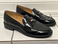 Side view of the pair of black patent penny loafers showing glossy finish and classic loafer design with low heel.