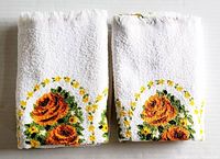 Two vintage unused white guest towels with orange and yellow rose floral designs and green leaves, folded and laid side by side showing floral design on lower edges.