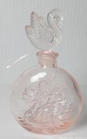 Front angle of vintage pink glass perfume bottle with swan stopper showing embossed swan on body and visible crack.