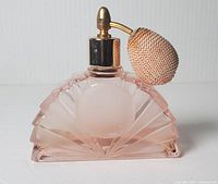 Front view of pink frosted Art Deco style perfume bottle with fan-shaped geometric design and attached fabric-covered atomizer bulb spray with brass nozzle.