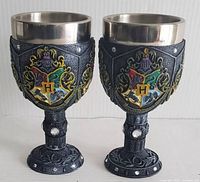 Two Harry Potter goblets with Hogwarts crest front view showing colored emblem and textured black base with gem accents and metallic rims.