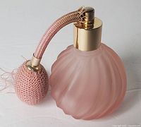 Full view of vintage pink frosted glass perfume bottle with atomizer bulb and gold-tone cap.