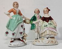 Front view of two vintage hand painted porcelain figurines: a maid with basket and dog, and a couple in period clothing.