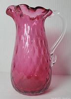 Full side view of cranberry glass pitcher showing textured pattern and ruffled top edge.