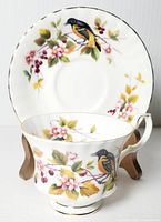 Photo of teacup in front of the saucer showcasing Baltimore Oriole bird and floral design with gold trim on fine bone china.