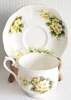 Fine bone china teacup and saucer with yellow primrose floral design, front angle showing cup handle and saucer floral pattern