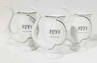 Photo of three white porcelain hot beverage cups with unique curved handles and silver detailing. Cups display Grandhotel Pupp Karlovy Vary on front.
