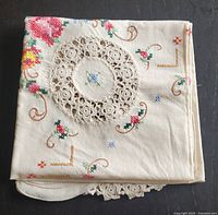 Folded vintage cotton blend square table accent with floral embroidery and central crochet lace detail showing scalloped edges