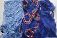 Three scarves laid flat showing variety in color and pattern: light blue embroidered, royal blue patterned, and solid deep blue.