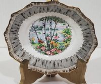 Front view of the small oval porcelain dish with a central image of birch trees and colorful flowers, bordered by a birch bark pattern rim with gold scalloped edge.