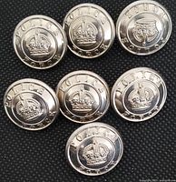 Group of seven round silver Police Force buttons arranged on black textured background showing embossed crowns and text