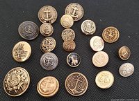 Full view of 21 assorted antique brass buttons showing various sizes and designs including anchors, lions, and crests.