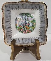 Front view of square dish with birch tree and floral scene in center, gold trim on rim