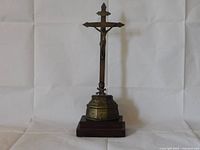 Front view of the brass crucifix mounted on the wooden base showing the figure of Christ and engraved base.