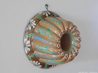 Side angle view of the vintage hand-painted Alsace pottery kougelhopf mold showing floral and leaf patterns and metal hanger.