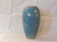 Front view of tall, blue, glossy porcelain vase with gold rim, against white fabric background.