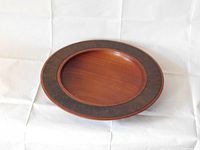 Front angle top view of circular wood fruit bowl showing natural wood grain outer edge with dark carved textured band around rim and smooth bowl center.
