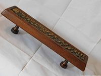 Angled side view of rectangular bronze and teak door pull showing bronze geometric relief and one mounting post.