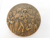 Front side of bronze medallion depicting historical figures, ships, and coats of arms with Portuguese inscription.