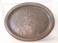 Front view of oval tin tray showing full embossed design with parasols, fans, maple leaves on aged patinated metal surface.