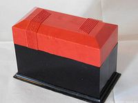 Side view of vintage Art Deco card box featuring red lid with ribbed design and black base on stepped black platform.