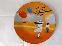Full view of the round enamel on copper painting showing the girl with balloons against orange sky with bats and tree branches.