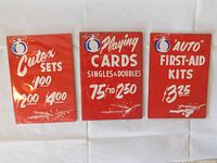 Three vintage red Honest Ed's Christmas hand-painted signs displayed side by side, showing advertisements for Cutex Sets, Playing Cards, and Auto First-Aid Kits with festive Christmas balls and decorative details.