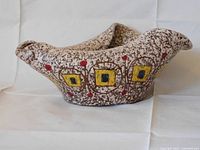 Front and side view of the irregular handmade pottery bowl showing textured glazing and geometric yellow square designs with red dot accents.