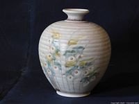 Front angled view of a rounded ceramic vase with narrow neck, floral decoration and textured ribbed surface.