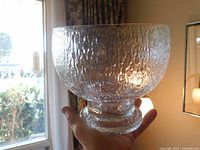 Clear view of the bowl held in hand showing size, heavy base, and textured ice pattern on the glass surface.