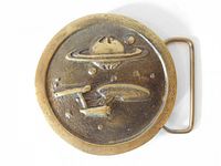 Front view of the original cast brass Star Trek belt buckle showing raised USS Enterprise spaceship and planet design.