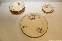 View of all 13 pieces laid out on a white tablecloth showing floral pattern and gold edging.