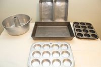 Full set of baking pans: one tube pan, two loaf pans, one large rectangular pan, one metallic muffin tin and one non-stick muffin tin arranged on a table.