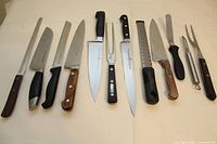 Full view of the set of 11 kitchen utensils including 8 knives, carving fork, grater, peeler, and spatula spread on a flat surface