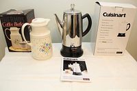 Photo showing Cuisinart coffee percolator with black handle and base, insulated Coffee Butler with floral design, their boxes, and instruction manual on a white surface.