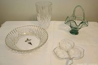 Full view of the four collectible vintage glassware items on a white cloth: clear lead crystal vase with pineapple pattern, green glass basket with handle, maple leaf divided dish, and round clear plate.