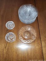 Ten clear crystal plates stacked showing a mix of cut and etched patterns, next to two clear cut glass round ashtrays with starburst and swirl design.