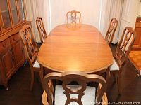 Photo showing the large wooden dining table with scalloped edges and six matching chairs with decorative backs and upholstered seats.