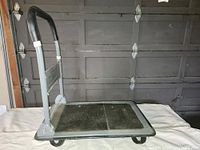 Full view of folding wheeled utility cart with handle extended and black rubber mat surface.