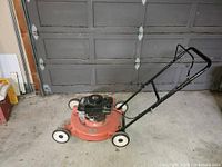 Full view of orange gas lawn mower with black handle in garage setting.