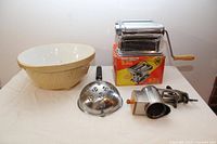 Full view of pasta machine with original box, ceramic bowl, pasta ladle, and cheese grater.