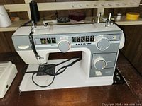 Close-up photo of Janome L372 sewing machine mounted in cabinet, showing control dials and stitch pattern panel.