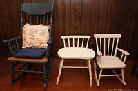 Full view of three chairs: adult black rocking chair with cushions, light wood child's rocking chair, and small wooden stool