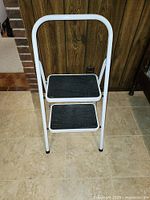 Front view of the white collapsible two-step stool showing black rubber treads on each step.