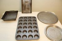 Top-down view of all five baking pans laid out on table showing muffin pan with 24 cups, rectangular and square pans, round pie pan, and round cookie sheet.