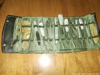 Full view of vintage grooming and manicure set in green fabric roll-up case showing all tools neatly secured in elastic loops.