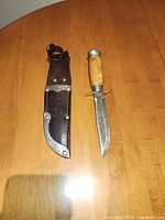 Photo of the vintage Mora cutting utensil and its leather sheath side by side on a wooden surface, showing overall appearance.